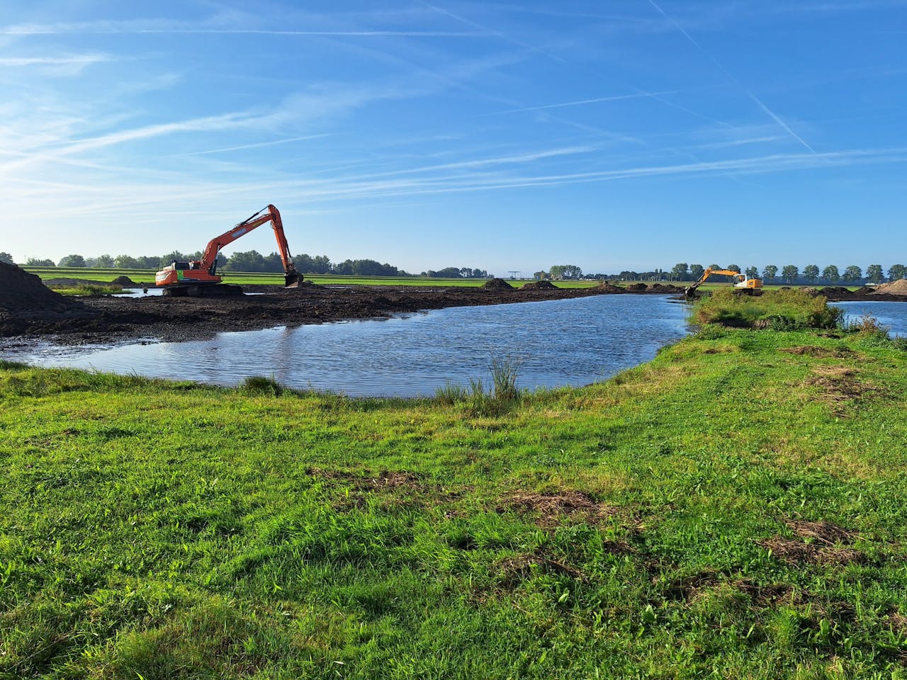 Greppelveld met grasland, graafmachines en nieuwe waterpartijen op een zonnige dag